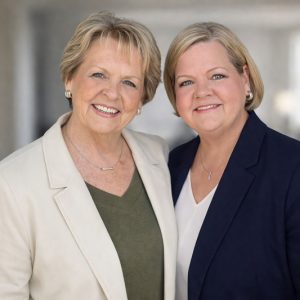 Two smiling professional women in blazers, friendly portrait with soft blurred background