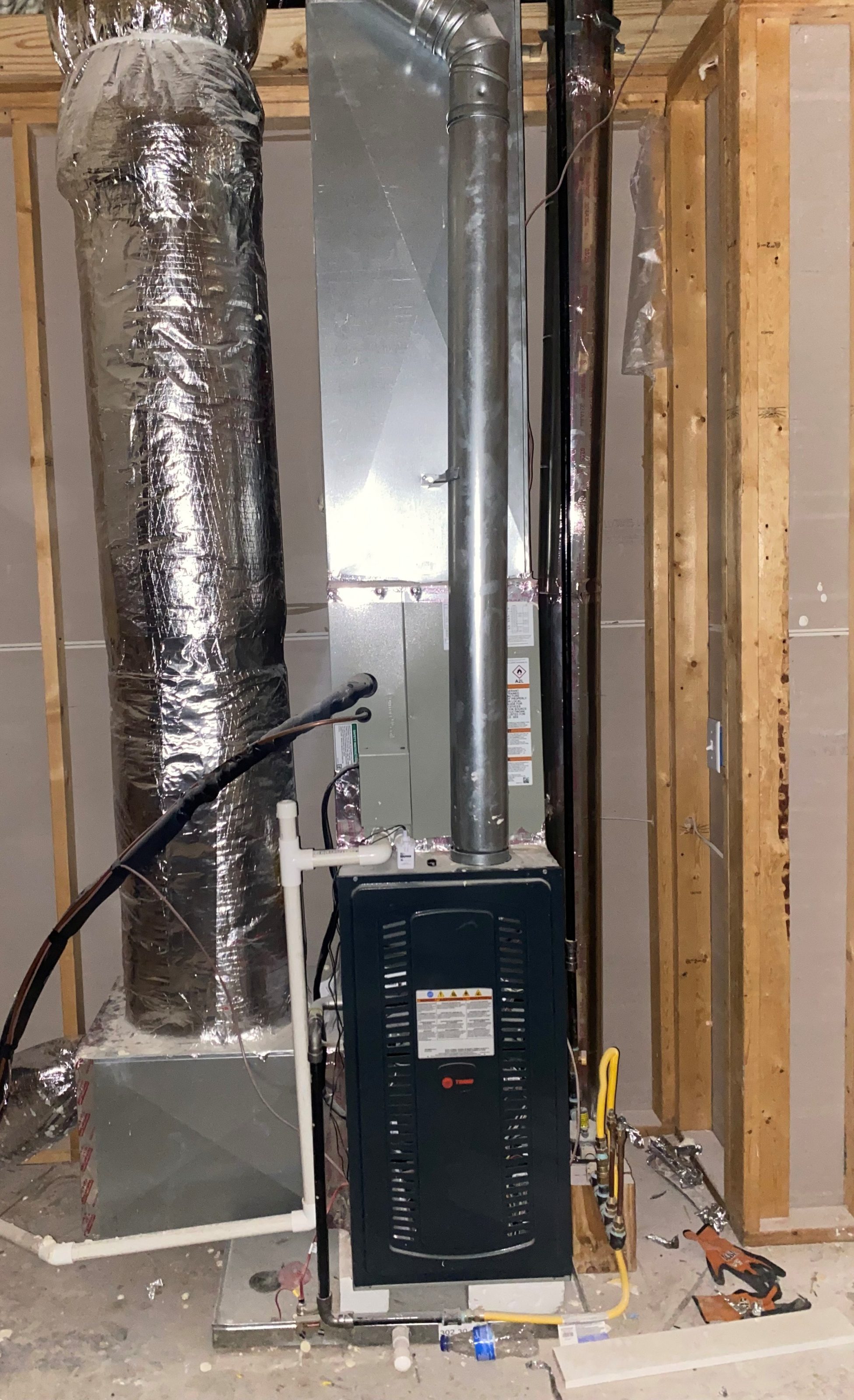 Residential HVAC furnace unit with insulated ductwork and exposed stud wall in unfinished basement.