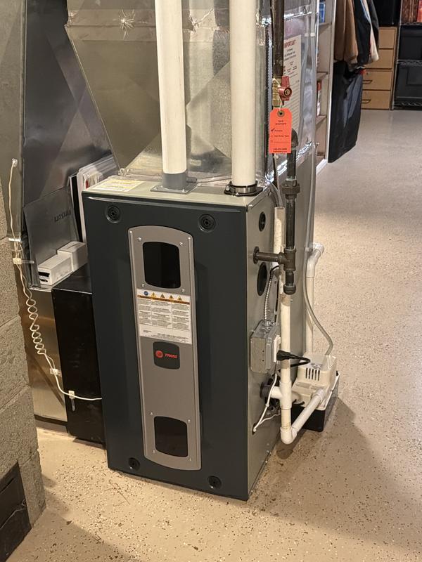 Trane furnace air handler with PVC condensate lines and adjacent ductwork in basement
